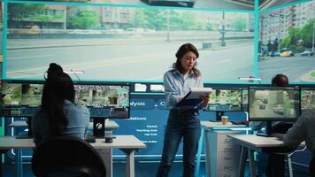 Manager overseeing employees in monitoring traffic activity, operating through surveillance footage on CCTV cameras. Diverse team work with satellite system in control center. Camera B. video