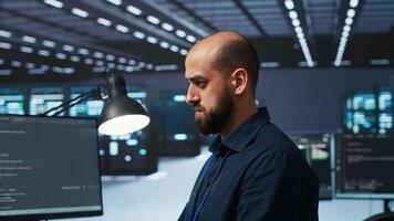 Programmer writing code, working in network security data center facility, ensuring optimal performance. IT specialist using PC to monitor energy consumption across operational server racks video