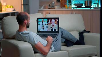 Comfortable man relaxing on couch while having online business conference with collegues using laptop computer during quarantine. Focused adult talking on videocall use webcam late at night in kitchen video