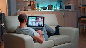 Caucasian male talking with collegues during call conference using laptop computer with modern technology wireless. Tired man relaxing on sofa late at night in kitchen video