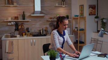 donna d'affari digitando su il computer portatile mentre Lavorando remoto in ritardo nel casa cucina. occupato focalizzata dipendente utilizzando moderno tecnologia Rete senza fili fare col tempo per lavoro lettura scrivere, ricerca video