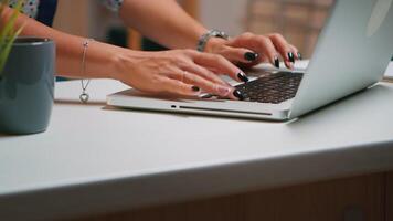 Close up of woman typing on laptop sitting in the kitchen late at night and working. Busy focused employee using modern technology network wireless doing overtime for job reading writing, searching video