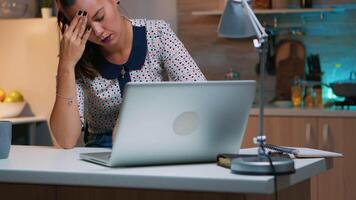 benadrukt bezig vrouw met hoofdpijn werken van huis laat Bij nacht Aan laptop. moe gefocust werknemer gebruik makend van modern technologie netwerk draadloze aan het doen na een tijdje voor baan lezing schrijven, zoeken video