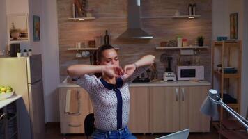 stanco donna d'affari streching mentre Lavorando col tempo a partire dal casa cucina. occupato focalizzata dipendente utilizzando moderno tecnologia Rete senza fili fare col tempo per lavoro lettura scrivere, ricerca video