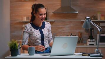 donna a distanza imprenditore avendo conferenza con colleghi utilizzando il computer portatile seduta nel il cucina in ritardo a notte. occupato dipendente utilizzando moderno tecnologia Rete senza fili fare col tempo per lavoro. video