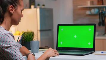 trabalhador autonomo olhando às verde tela monitor sentado às casa dentro cozinha. o negócio mulher assistindo Área de Trabalho computador portátil exibição com verde brincar, croma chave, durante noite Tempo trabalhando ao longo do tempo. video