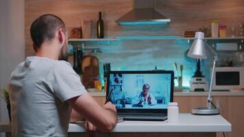 Male writing on notebook during online consultation listening woman doctor sitting in front of laptop in the kitchen. Sick man discussing during conference about symptoms holding bottle of pills video