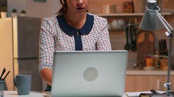 libero professionista digitando su il computer portatile in ritardo a notte seduta nel il cucina Lavorando a distanza. occupato focalizzata dipendente utilizzando moderno tecnologia Rete senza fili fare col tempo per lavoro lettura scrivere, ricerca video