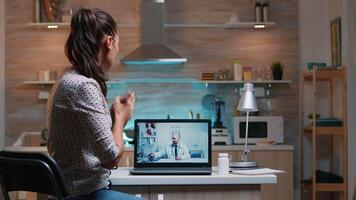 telemedicina consulta durante codicioso pandemia a noche, mujer sentado en frente de ordenador portátil en el cocina. enfermo dama que se discute durante virtual consulta acerca de síntomas participación botella de pastillas video