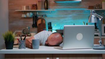 überarbeitet Mann Schlafen auf Küche Schreibtisch Arbeiten entfernt spät Std beim heim. beschäftigt erschöpft Fernbedienung Mitarbeiter Nickerchen machen auf Stuhl aufwachen oben Arbeiten auf Laptop mit modern Technologie Netzwerk im Laufe der Zeit video