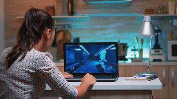 Woman gamer sitting at home in kitchen testing new game on professional laptop. Tired player gaming online games on her personal computer with modern technology network wireless video