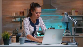 cansado mujer de negocios trabajando tiempo extraordinario Bebiendo café a hogar en moderno cocina. ocupado enfocado empleado utilizando moderno tecnología red inalámbrico exceso de trabajo para trabajo leyendo escribiendo, buscando. video