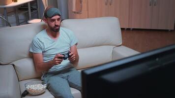 Spieler Mann halten kabellos Regler während spielen Videospiele während Quarantäne. Profi Spieler Sitzung im Vorderseite von Fernsehen auf Sofa Herstellung glücklich Geste spät beim Nacht im Küche video