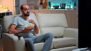 caucásico fútbol americano ventilador acecho su equipo victorioso el competencia, comiendo Palomitas. partido objetivo en vivo habitación tarde a noche, alegre puntuación ganar celebrando campeonato video