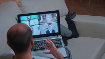 Back shot of tired man lying on sofa while chatting with teammates during business videocall conference use laptop computer. Caucasian male using modern technology wireless late at night in kitchen video