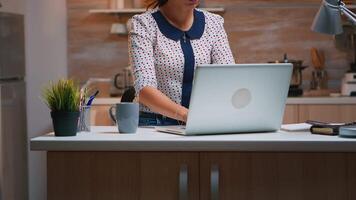 mujer bostezando mientras trabajando remotamente desde hogar tarde a noche en el cocina. ocupado agotado empleado utilizando moderno tecnología red inalámbrico haciendo tiempo extraordinario para trabajo leyendo mecanografía, buscando video