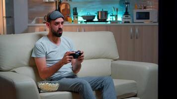 Defeat man playing games on television during online competition using gaming controller. Disappointed pro gamer sitting on couch upset for losing soccer game late at night in kitchen video