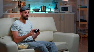 Frustrated pro gamer losing entertainment gaming competition using joystick. Serious man sitting on couch late at night in kitchen while playing online games on television video