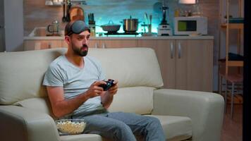 Pro gamer making winner gesture after winning entertainment videogame competition holding gaming controller. Focused man sitting in front on television on sofa late at night in kitchen video