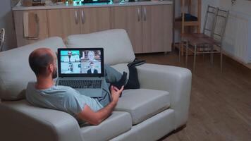 caucasian manlig talande handla om företag kommunikation projekt under ring upp möte använda sig av bärbar dator dator. fokuserade man liggande på soffa i pijamas använder sig av modern teknologi trådlös sent på natt video