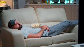 Man closing his eye and falling asleep on the couch in living room in front of the TV, while the television entertainment is ON. Relaxation cinema after a hard week of work video