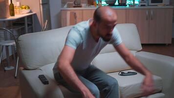 Porträt von konzentriert Mann Aufpassen Unterhaltung zeigt an Serie Sitzung auf Couch im Vorderseite von Fernsehen. kaukasisch männlich entspannend nach lange Tag beim Arbeit spät beim Nacht im Küche video