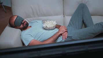 kaukasisch männlich fallen schlafend während Aufpassen Film Show Sitzung auf Couch spät beim Nacht im Küche. müde Mann tragen Auge Schlaf Maske während das Fernseher ist auf video