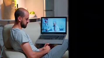 ziek Mens hebben online telegeneeskunde overleg gedurende covid19. Kaukasisch mannetje zittend in voorkant van laptop bespreken met medisch arts over ziekte symptomen werken Aan gezondheidszorg behandeling video
