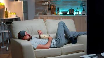 hombre acostado en sofá, que cae dormido en fron de el televisión con palomitas de maiz cuenco en su manos. cansado solo hombre en vivo habitación después un difícil día a trabajo video