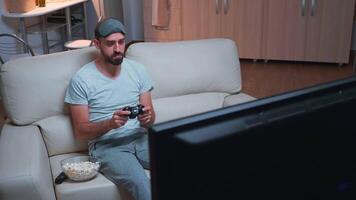 Disappointed gamer playing soccer videogame during gaming competition using joystick. Defeat man losing game while standing in front of television late at night in kitchen video