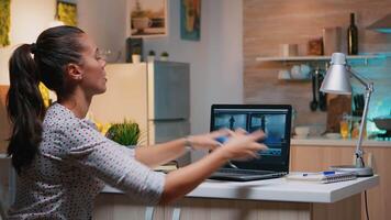 Freelancer content creator working overtime from home to respect deadline. Woman videographer editing audio film montage on professional laptop sitting on desk in modern kitchen in midnight video