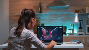 joven mujer jugador jugando en línea profesional juego en ordenador portátil a hogar tarde a noche. profesional jugador pruebas en línea juegos en su personal computadora con moderno tecnología red inalámbrico. video
