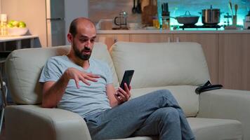 caucasiano masculino falando com dele colega sobre o negócio conferência usando telefone enquanto em pé dentro pijamas em sofá. cansado homem trabalhando atrasado às noite dentro cozinha usando moderno tecnologia sem fio video