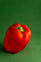 A shiny red pepper sits against a green backdrop, creating a vivid color contrast. The image highlights the pepper's smooth texture and rich hue, suggesting freshness and vibrancy. photo