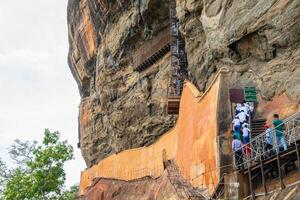Sigiriya, Sri Lanka - August-07-2019 - Group of tourist climbing staircase to visit the Mirror wall in Sigiriya. In the old days it was polished so thoroughly that the king could see his reflection. photo