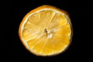 A cross-section of a dried lemon against a black background. The fading pulp and prominent membranes hint at aging, while the weathered texture adds depth to this close-up shot. photo