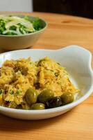 Bacalhau a Bras, a traditional Portuguese dish, served on a white plate in a restaurant setting. The shredded cod is mixed with eggs, crispy potatoes, parsley, and black olives. photo