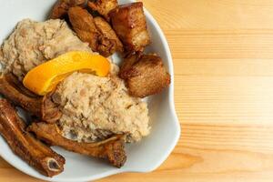 A plate of fried pork with Alentejo-style migas, a dish made from breadcrumbs, garlic, and herbs, topped with an orange slice. Captured in a rustic restaurant setting, it exudes warmth and tradition. photo