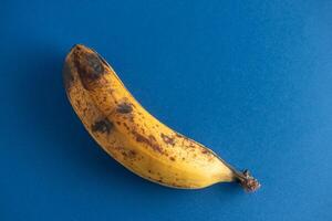 Old and wilted banana against a blue background. Symbolizes aging and decay. Perfect for illustrating concepts of impermanence. photo