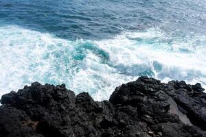 Idyllic scene of clear blue sea crashing against volcanic black rocks along the cliffs of Terceira Island, Azores. photo