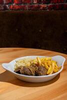 A plate of stewed black pork cheeks, paired with white rice and crispy French fries, displayed in a restaurant setting. This traditional Portuguese dish is a warm and hearty meal photo