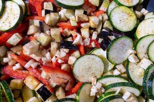 Chopped zucchini, red bell pepper, and eggplant, sliced and diced for sauteing. These fresh vegetables, with their vibrant colors, are neatly arranged on a white surface, ready for cooking. photo