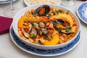 A traditional Alentejo restaurant serves a vibrant seafood feijoada. This dish features prawns, shellfish, and beans in a rustic clay pot, offering a hearty and authentic Portuguese experience. photo