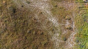 Aerial view of an abandoned soccer field. A lone goalpost stands amidst overgrown grass. Circular motorbike tracks crisscross the field, indicating where nature and human activity intersect. photo