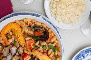 A traditional Alentejo restaurant serves a vibrant seafood feijoada. This dish features prawns, shellfish, and beans in a rustic clay pot, offering a hearty and authentic Portuguese experience. photo