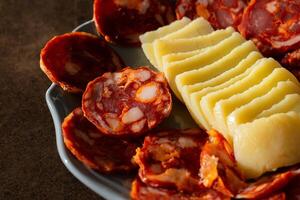 A traditional Alentejo sausage, known as paio, sliced and displayed alongside a rustic cheese wheel on a white plate in a charming restaurant setting. photo