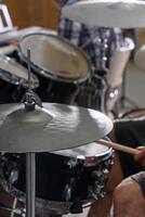 Close-up of a man's hands playing drums. His drumsticks hit with energy, showing the rhythm and motion of live performance. Cymbals and drumheads are slightly blurred, indicating movement. photo