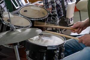 Close-up of a man's hands playing drums. His drumsticks hit with energy, showing the rhythm and motion of live performance. Cymbals and drumheads are slightly blurred, indicating movement. photo