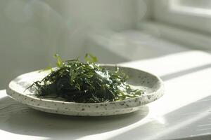 A plate with green salad made from chukka seaweed on a wooden table, illuminated by bright sunlight. Vegan seafood. photo