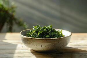 A plate with green salad made from chukka seaweed on a wooden table, illuminated by bright sunlight. Vegan seafood. photo